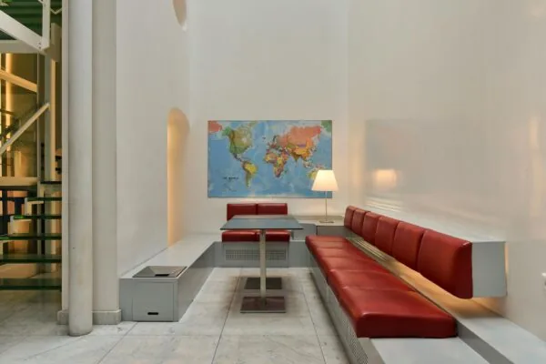 Moderne wachtruimte met rode banken, een wereldkaart aan de muur en een tafellamp op Rapenburg 139 in Leiden.