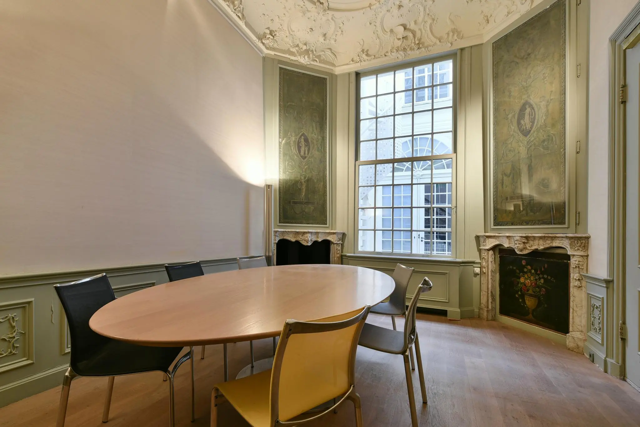 Vergaderruimte aan het Rapenburg met een ovaal houten vergadertafel, moderne stoelen, hoge ramen en historische wand- en plafonddecoraties.