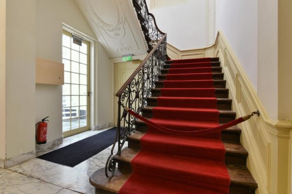 Trappenhuis met rode loper en sierlijke leuning in een klassiek gebouw aan het Rapenburg.