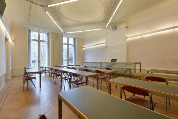 Licht klassieke collegezaal aan het Rapenburg met houten vloer, hoge ramen en moderne verlichting.