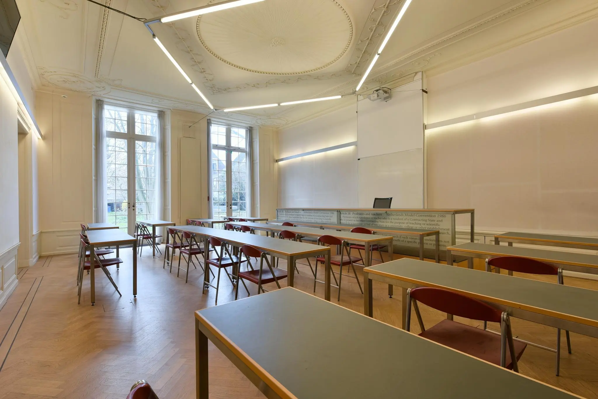 Licht klassieke collegezaal aan het Rapenburg met houten vloer, hoge ramen en moderne verlichting.