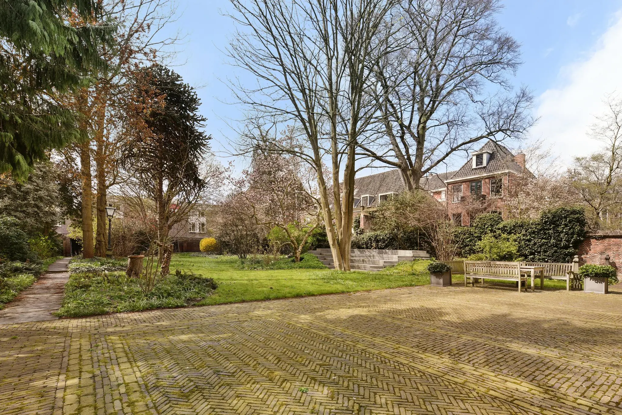 Grote, groene stadstuin aan het Rapenburg met oude bomen, zitbanken en een monumentaal pand op de achtergrond.