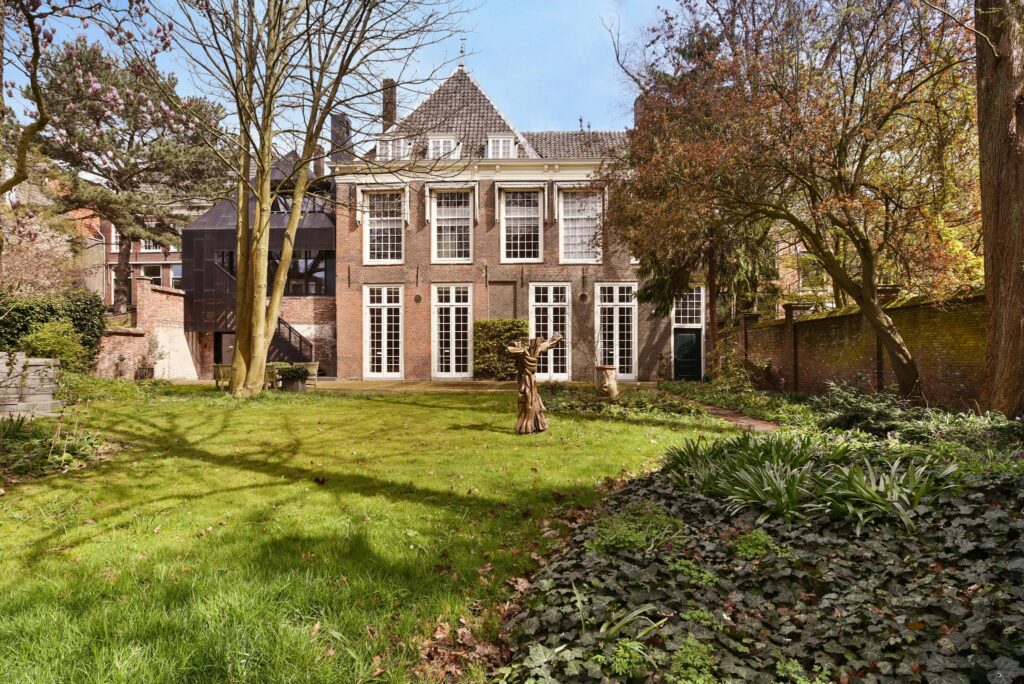 Achtergevel van een historisch pand aan het Rapenburg met grote ramen en een ruime tuin met bomen en struiken.