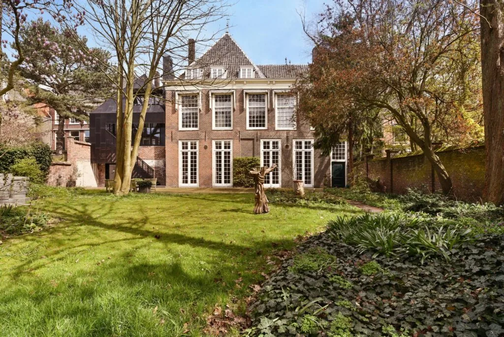 Achtergevel van een historisch pand aan het Rapenburg met grote ramen en een ruime tuin met bomen en struiken.