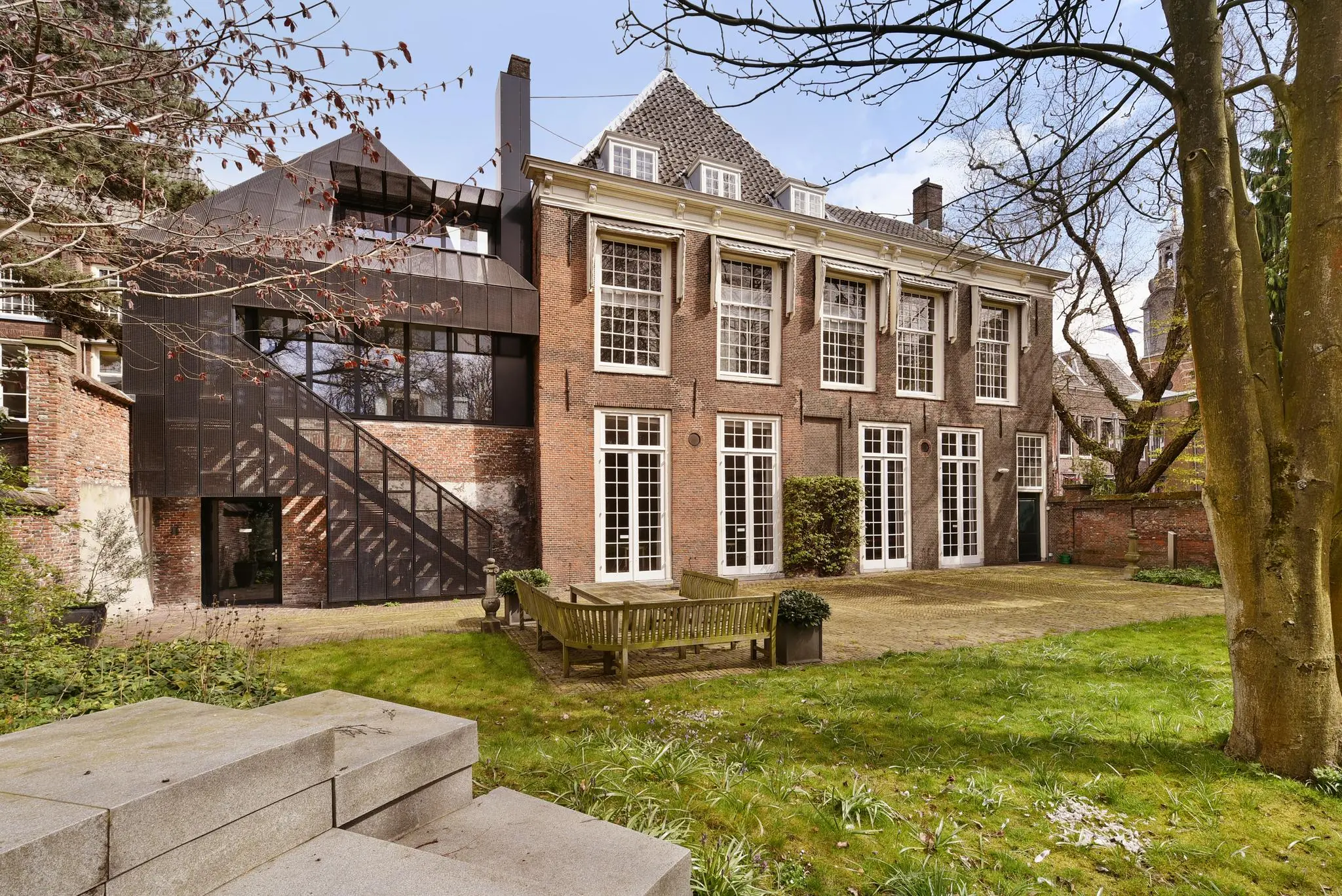 Achteraanzicht van een historisch pand aan het Rapenburg met een moderne aanbouw en een groene tuin met zitgelegenheid.