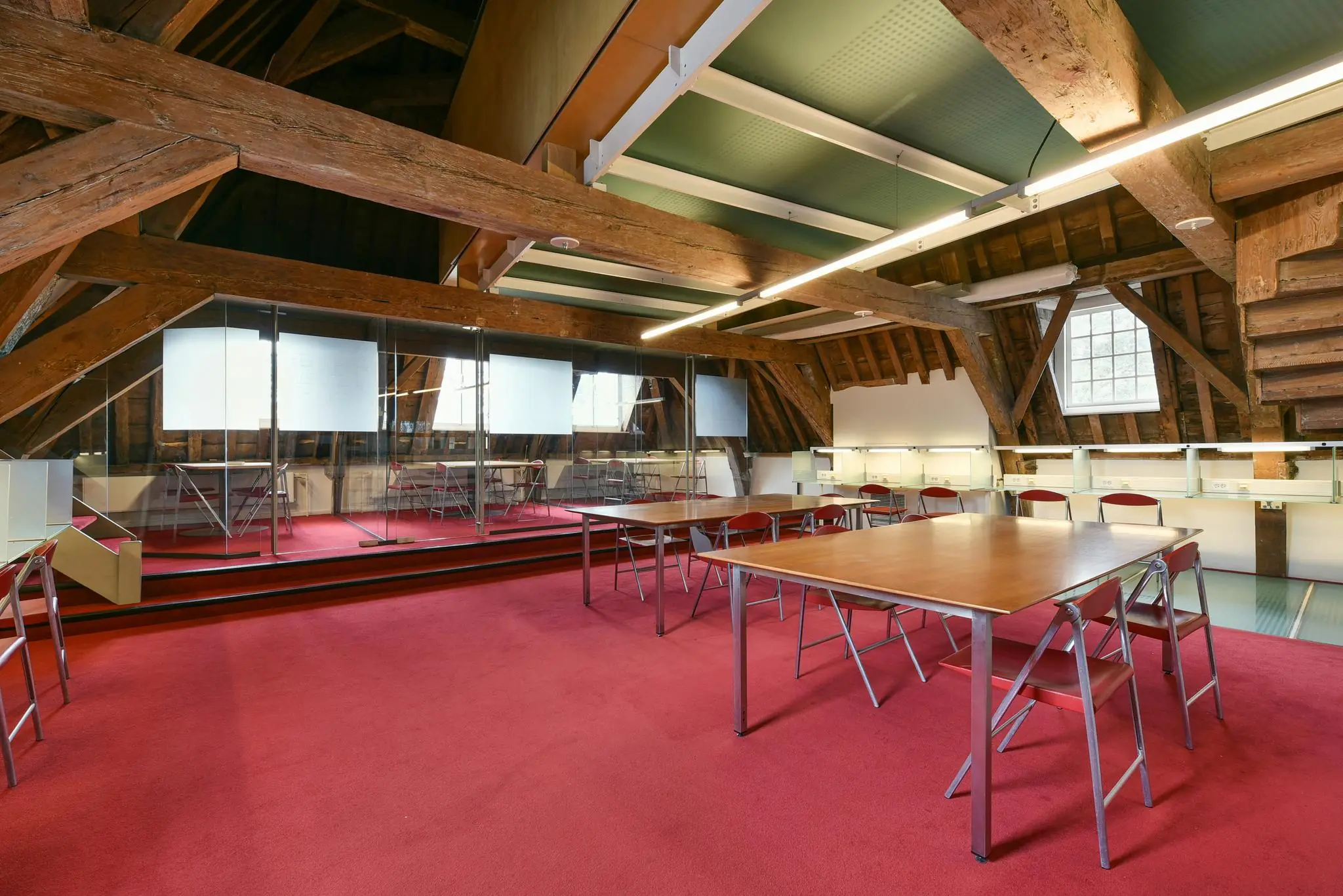 Lesruimte op de zolderverdieping van een historisch pand aan het Rapenburg, met houten balken, glazen wanden en rode vloerbedekking.