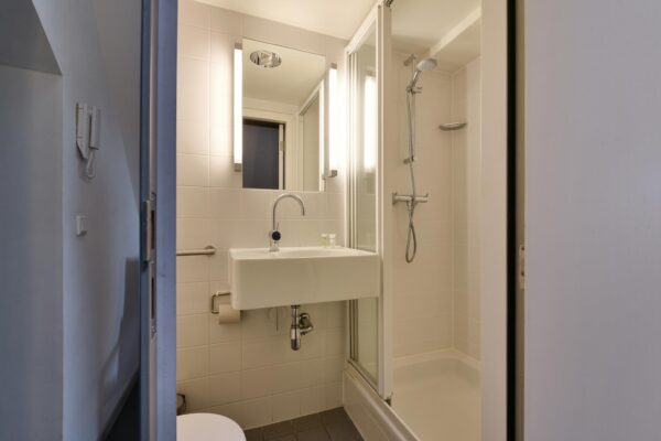 Moderne, compacte badkamer met douchecabine, wastafel en verlichte spiegel in een woning aan het Rapenburg.