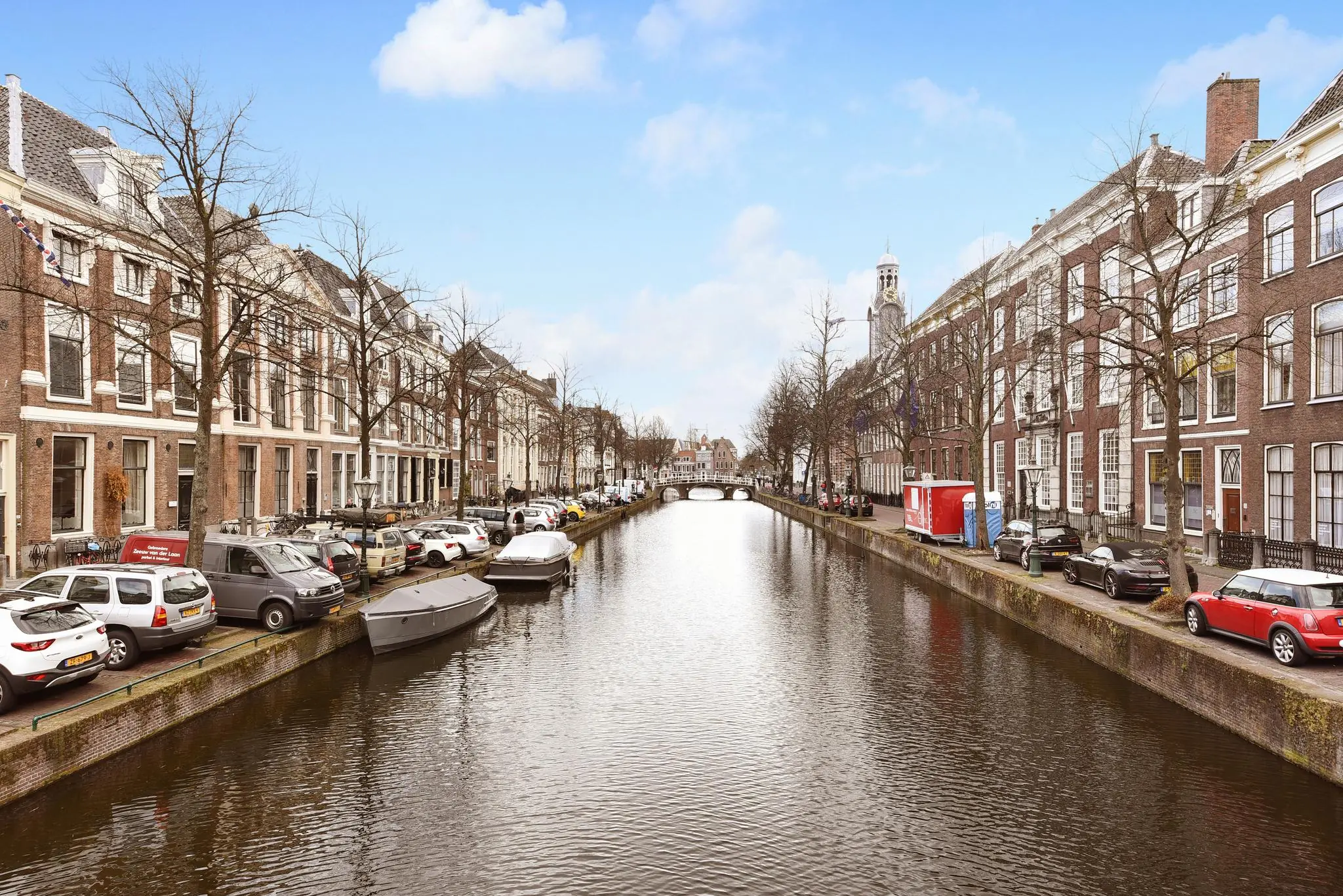 Gezicht op de Rapenburggracht in Leiden met historische panden, geparkeerde auto's en boten langs de kade.