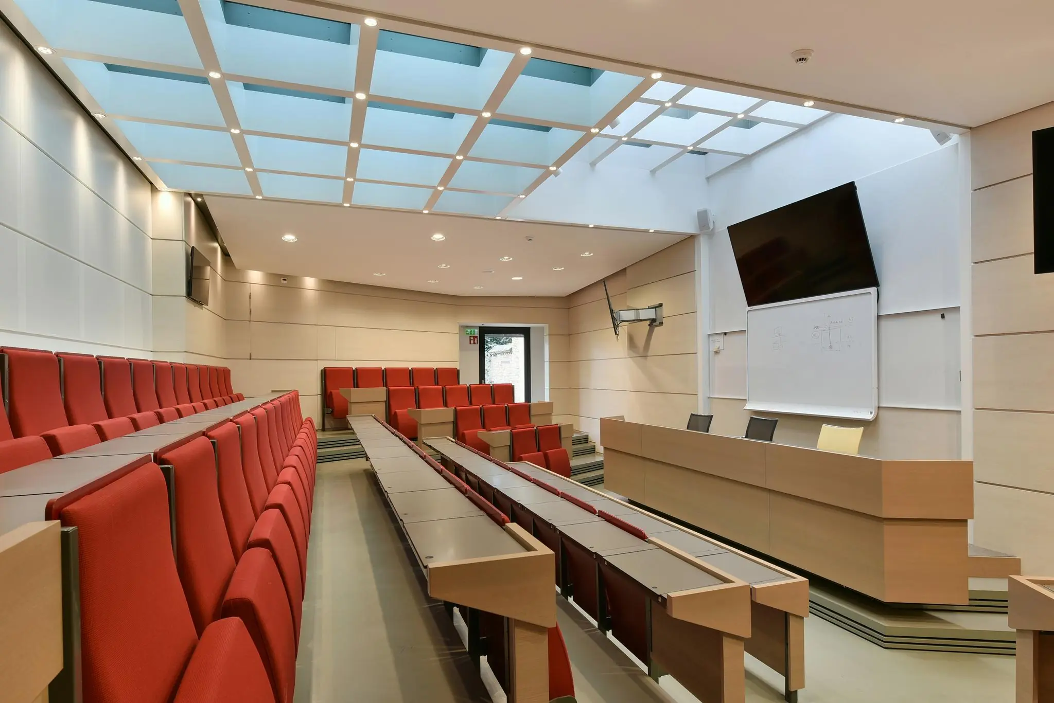 Moderne collegezaal aan het Rapenburg met rode stoelen, een licht plafond en een presentatiescherm boven het whiteboard.