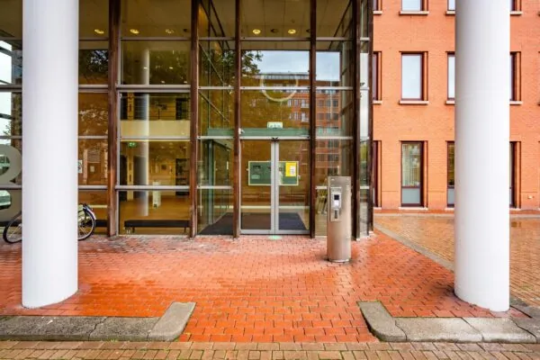 Ingang van een modern kantoorpand aan het Maanplein met glazen deuren, rode bakstenen en een toegangszuil.
