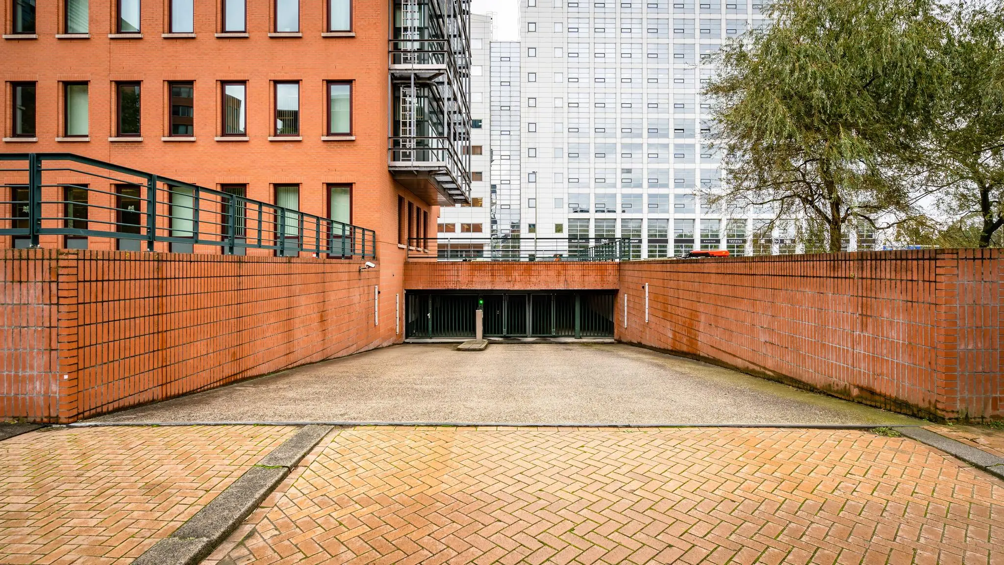 Inrit naar een ondergrondse parkeergarage aan het Maanplein, omringd door rode bakstenen muren en kantoorgebouwen.