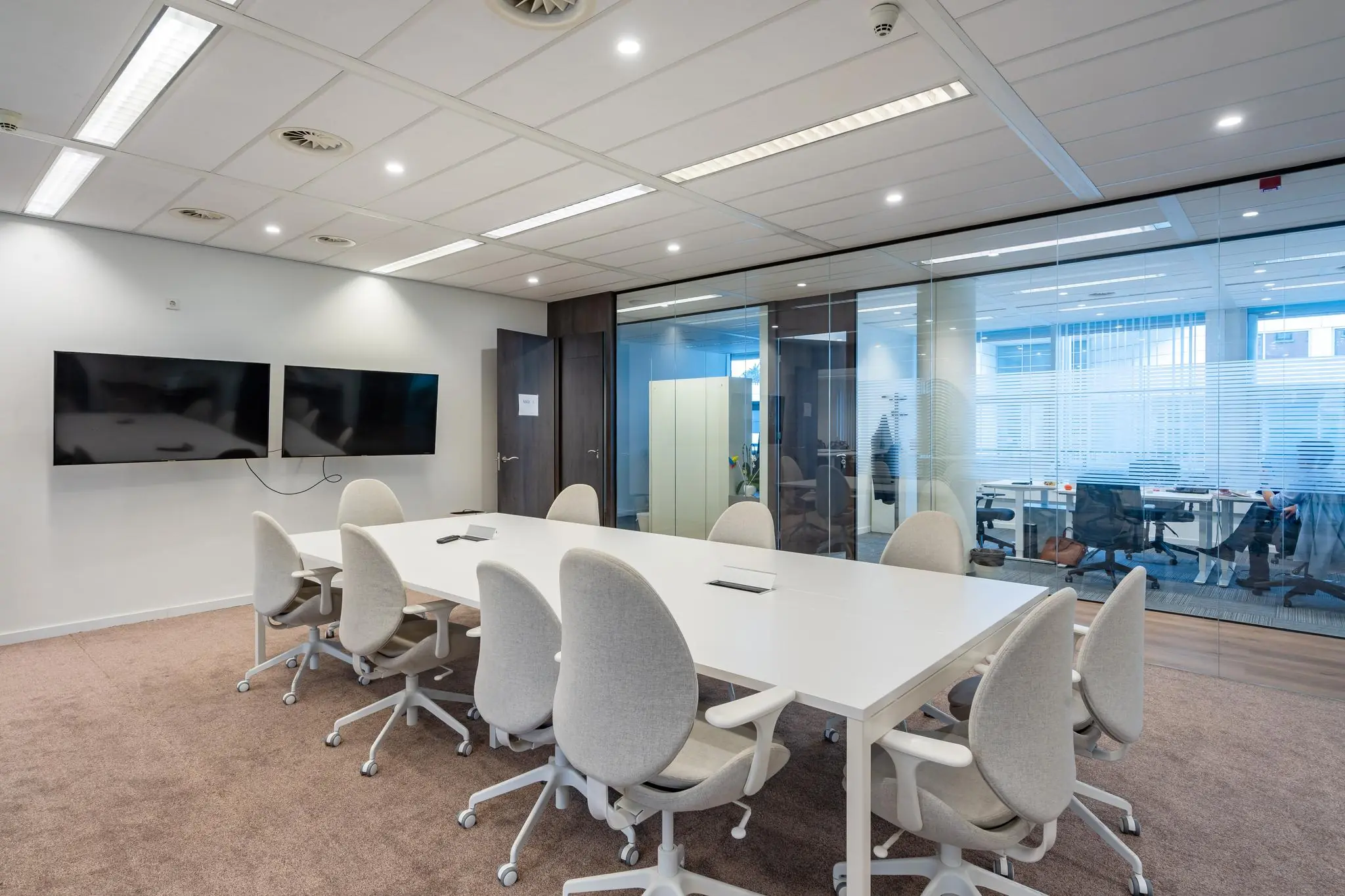 Vergaderruimte in kantoorpand Maanplein met witte tafel, grijze stoelen en twee schermen aan de muur.
