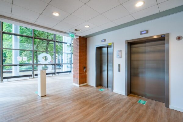 Moderne liftlobby op de achtste verdieping van een kantoorgebouw aan het Maanplein met twee gesloten liften en grote ramen met uitzicht op groen.