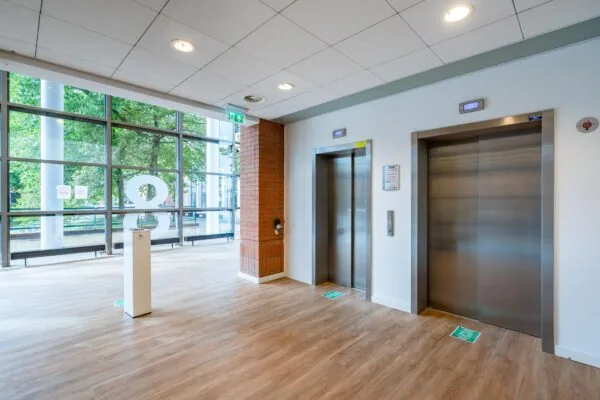 Moderne liftlobby op de achtste verdieping van een kantoorgebouw aan het Maanplein met twee gesloten liften en grote ramen met uitzicht op groen.