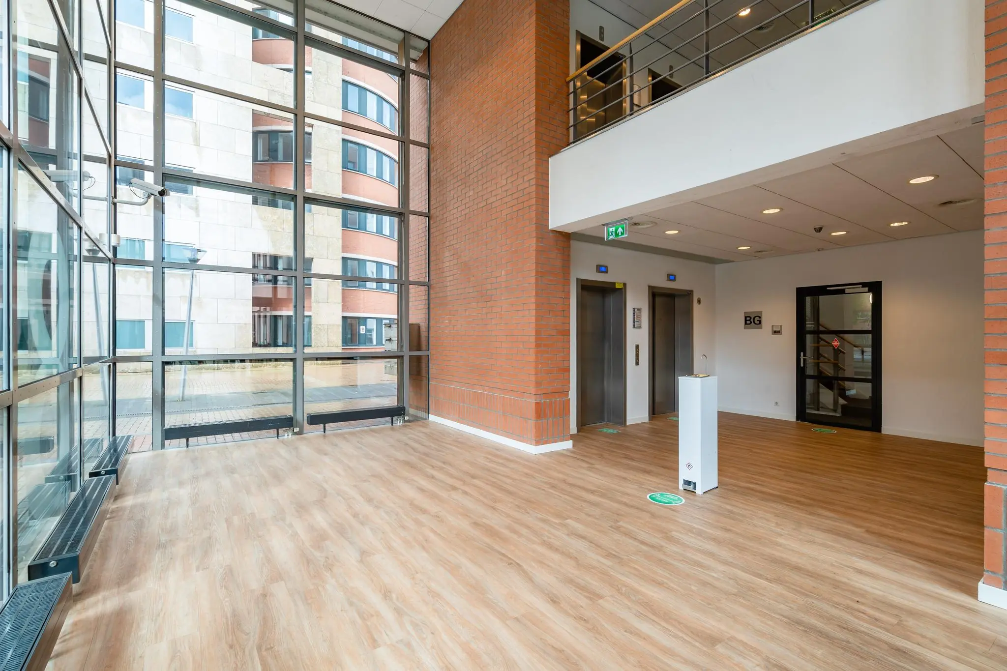 Moderne entreehal van een kantoorpand aan het Maanplein met houten vloer, twee liften en grote ramen met uitzicht op het naastgelegen gebouw.