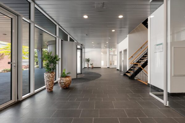 Moderne en lichte entreehal van een kantoorgebouw in Trondheim met grijze vloertegels, glazen deuren en planten in sierpotten.