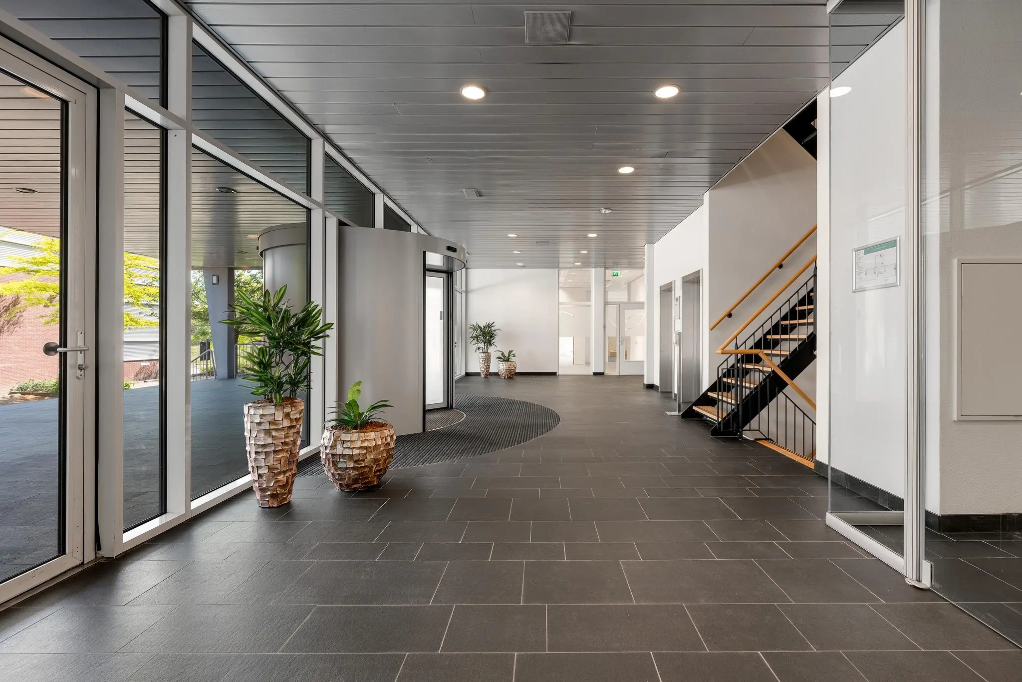 Moderne en lichte entreehal van een kantoorgebouw in Trondheim met grijze vloertegels, glazen deuren en planten in sierpotten.