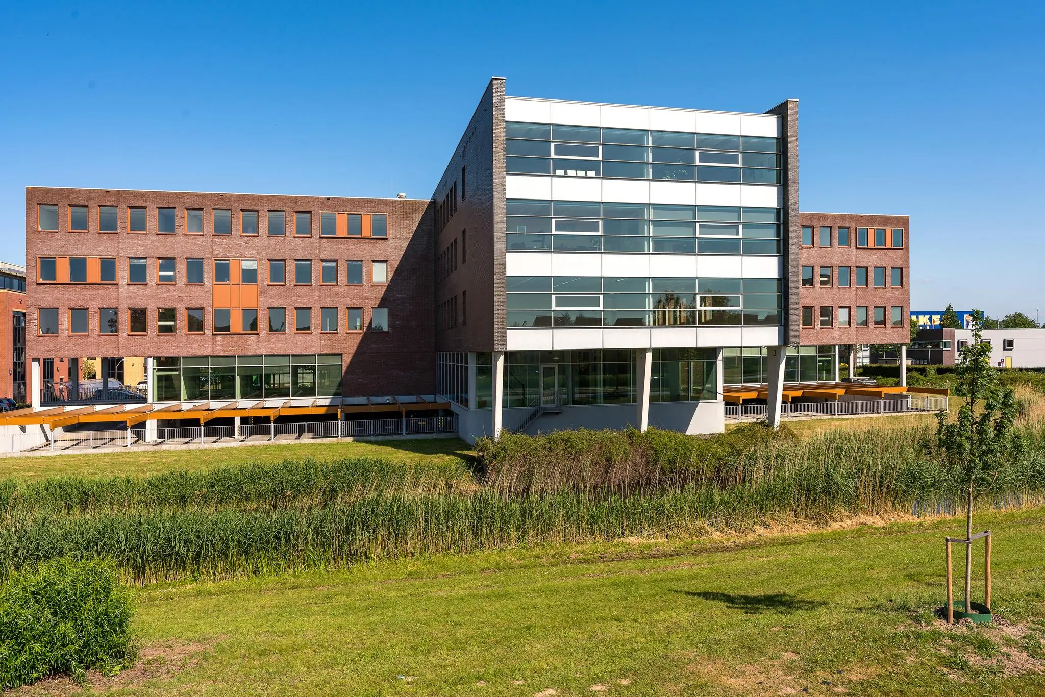 Modern kantoorgebouw in Trondheim met een combinatie van bakstenen en grote glazen gevels, gelegen aan een grasveld met riet.