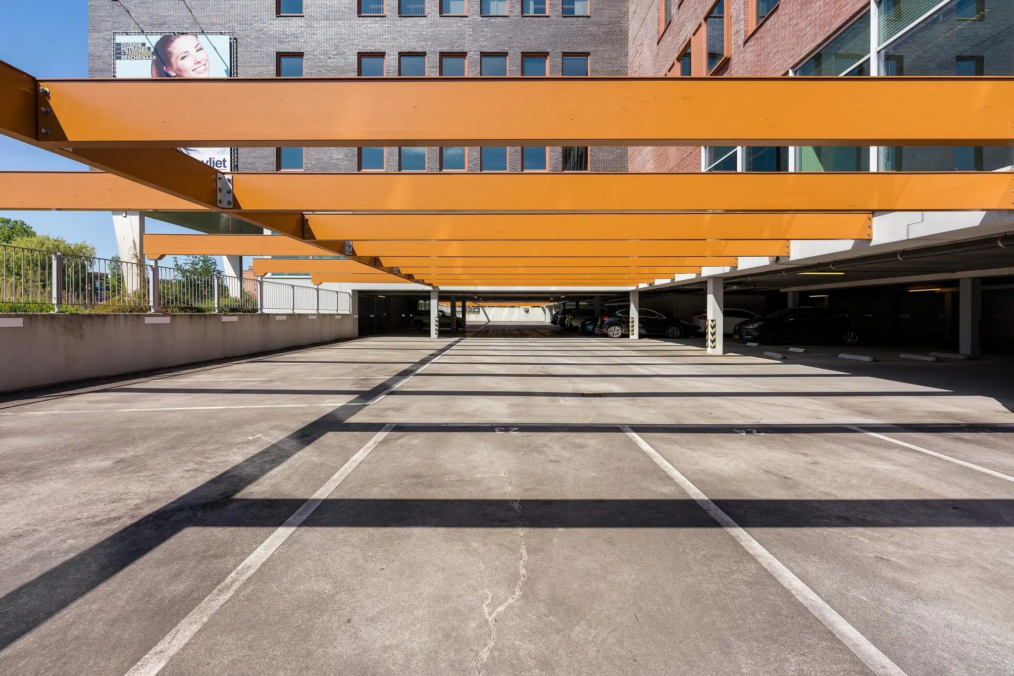 Openlucht parkeerplaats in Trondheim met opvallende oranje zonwerende balken en een deels overdekt parkeergedeelte.