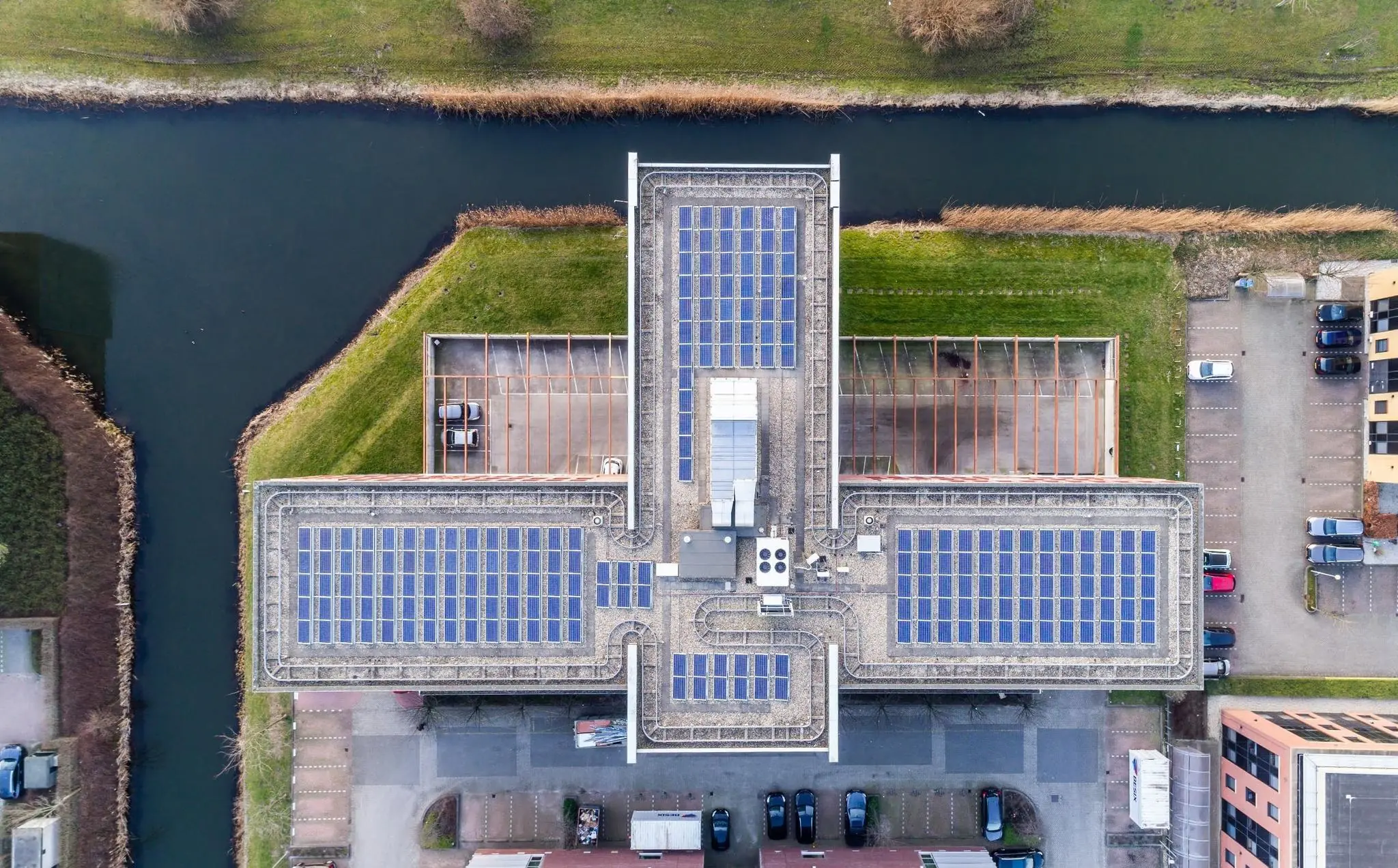 Luchtfoto van een T-vormig gebouw in Trondheim met zonnepanelen op het dak, omringd door groen en water.