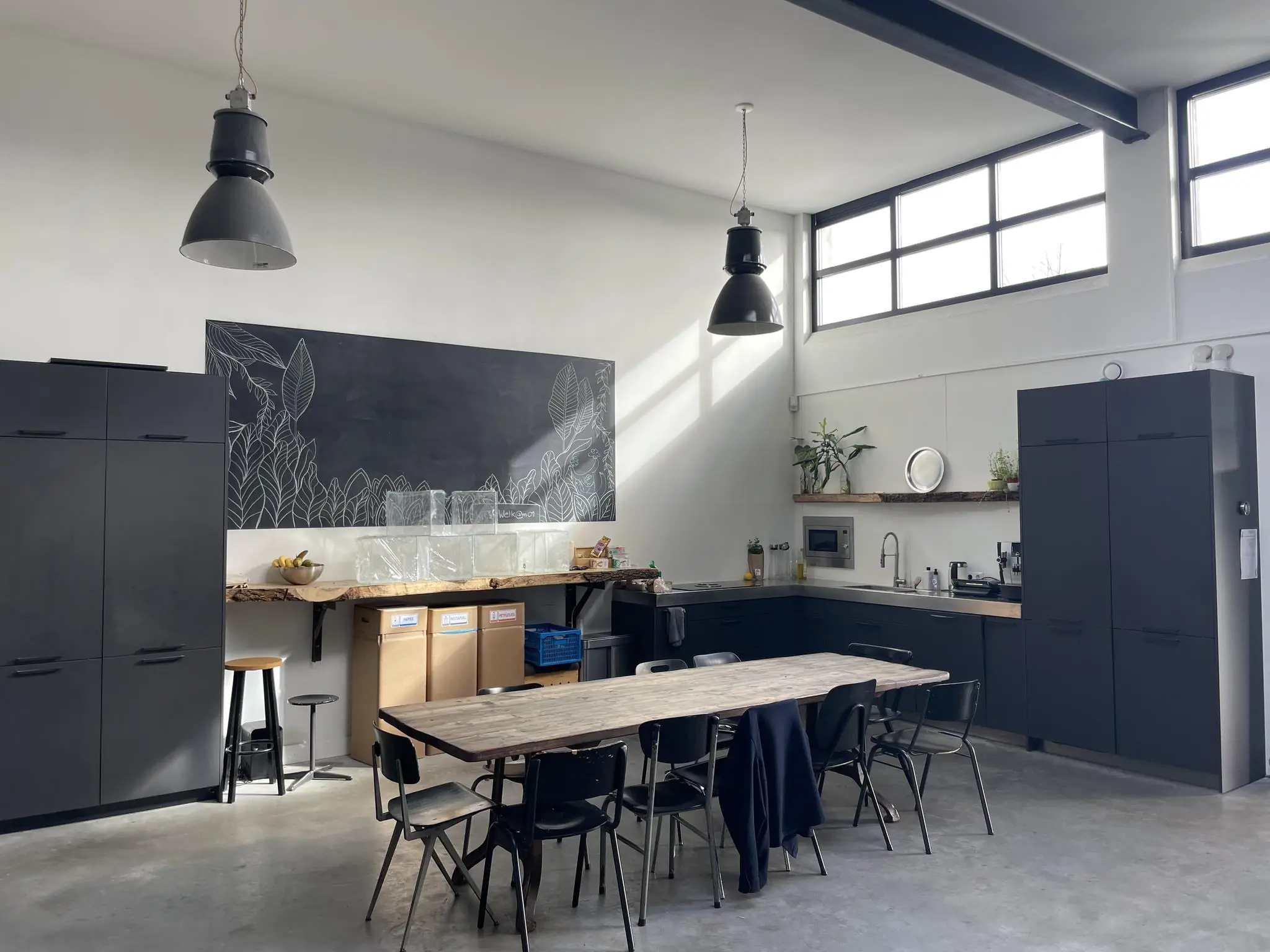 Moderne, industriële keuken met donkere kasten, een houten eettafel en een grote zwarte schoolbordmuur met witte bladillustraties.