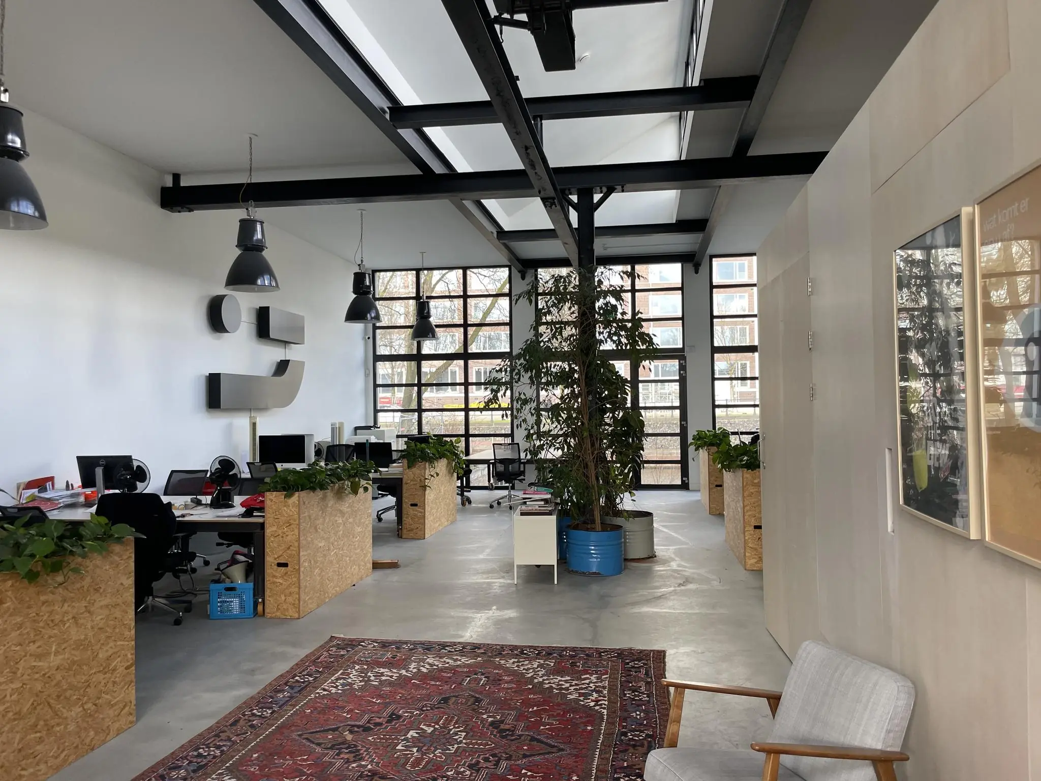 Moderne, open kantoorruimte aan de Veemarkt met houten bureaus, grote ramen en veel planten.