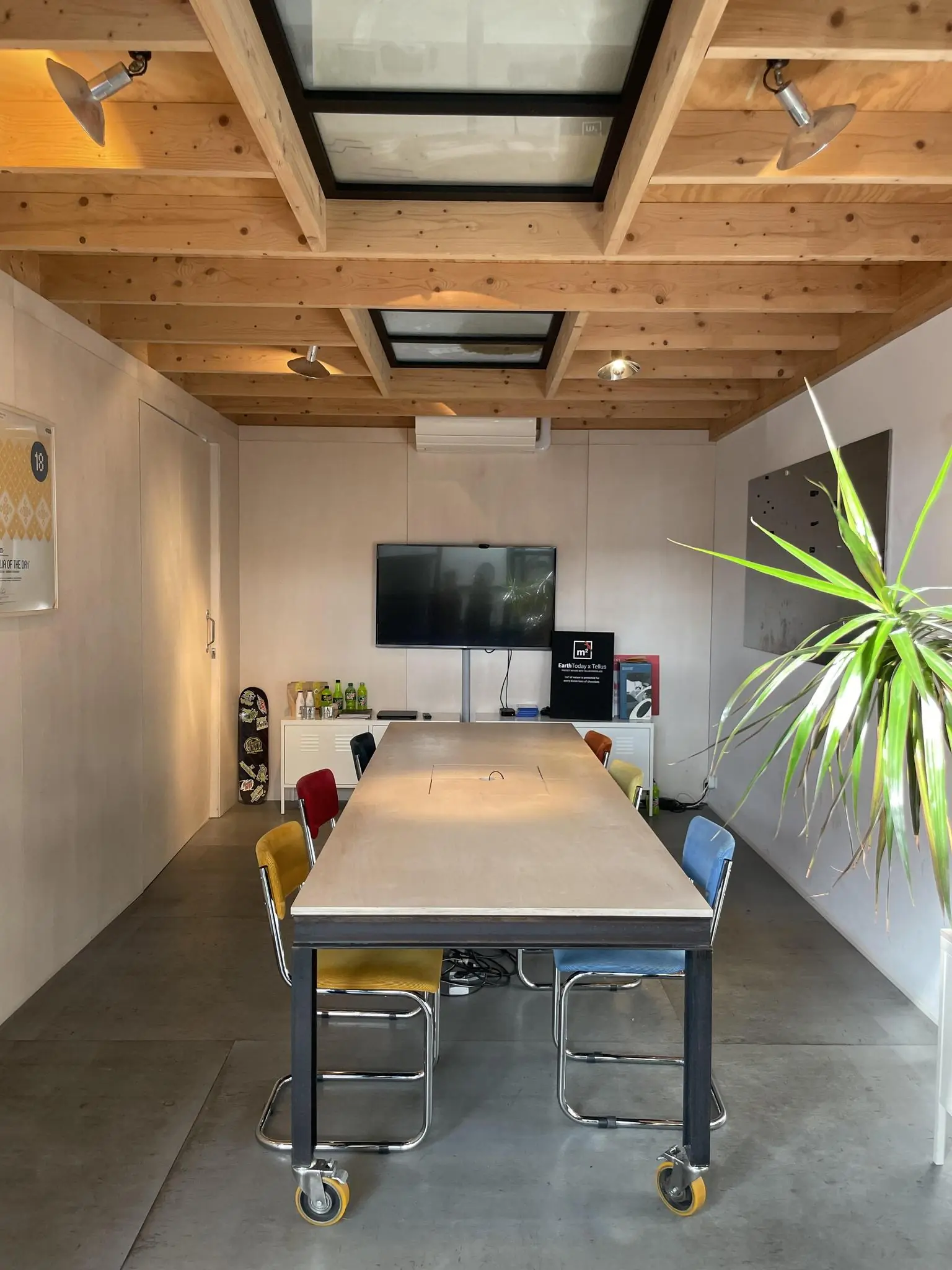 Vergaderruimte in een modern houten interieur met een lange tafel, kleurrijke stoelen en een flatscreen aan de muur.