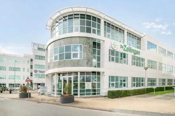 Modern kantoorgebouw van zorgorganisatie De Zellingen aan het Rhijnspoor, met glazen gevel en omliggende bestrating.
