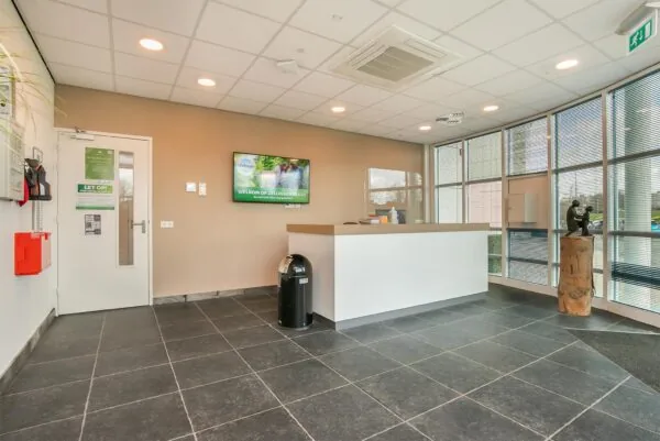 Moderne ontvangsthal van Rhijnspoor met balie, informatiescherm en glazen gevel.