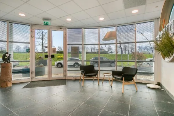 Moderne entree met zitgedeelte, grote ramen en uitzicht op geparkeerde auto's bij Rhijnspoor.