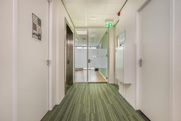 Gang in een modern kantoorgebouw met deur naar vergaderruimte genaamd "Spoorkamer 2".