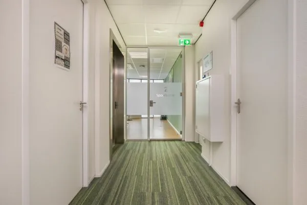 Gang in een modern kantoorgebouw met deur naar vergaderruimte genaamd "Spoorkamer 2".