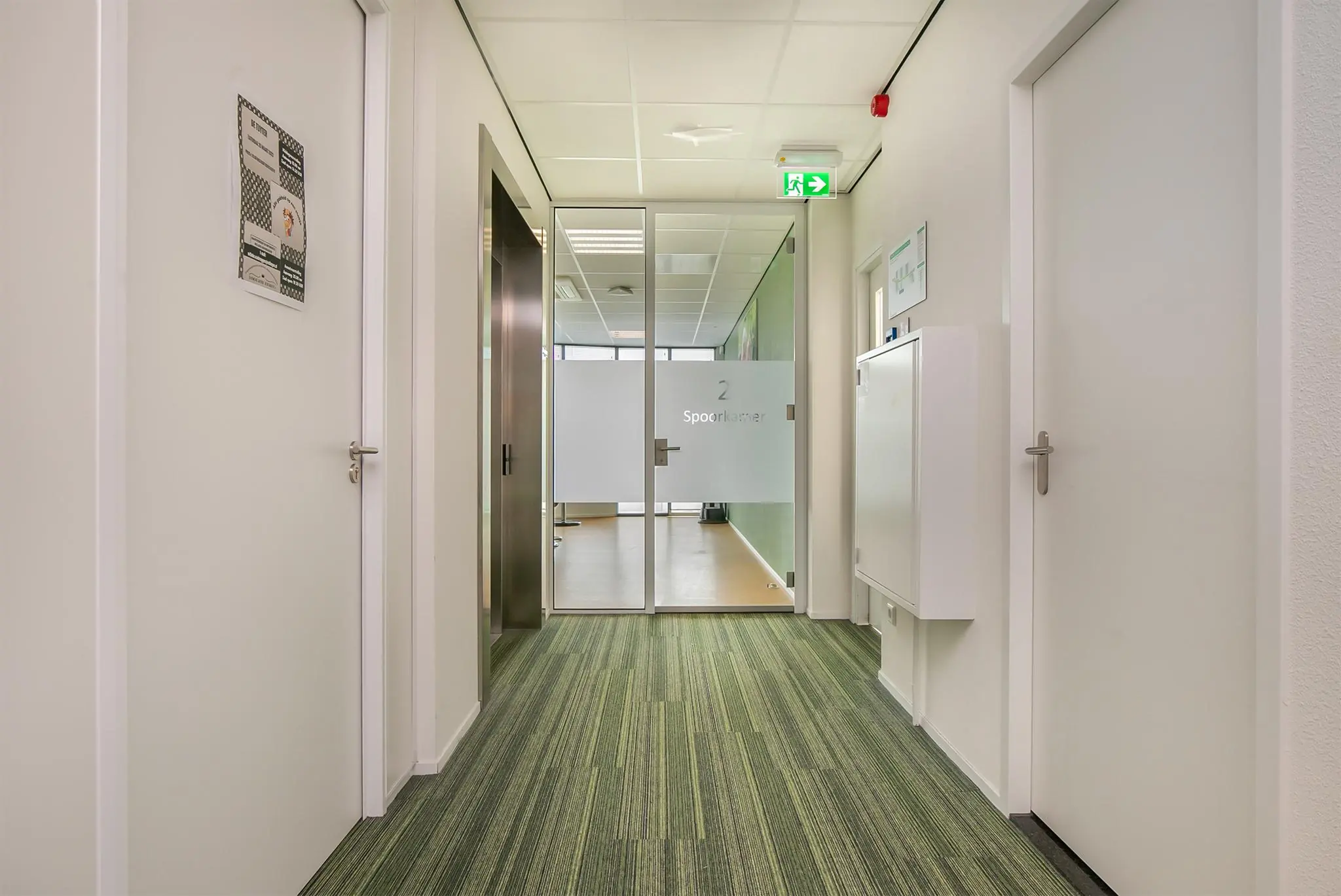 Gang in een modern kantoorgebouw met deur naar vergaderruimte genaamd "Spoorkamer 2".
