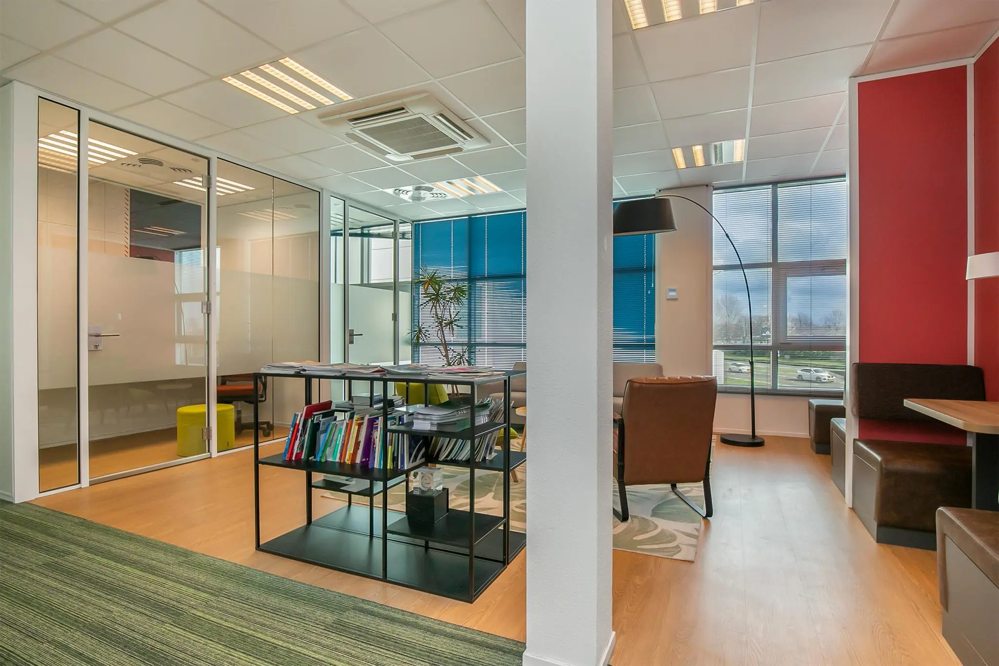 Modern kantoorinterieur aan het Rhijnspoor met glazen vergaderruimtes, een zitgedeelte en een open boekenkast.