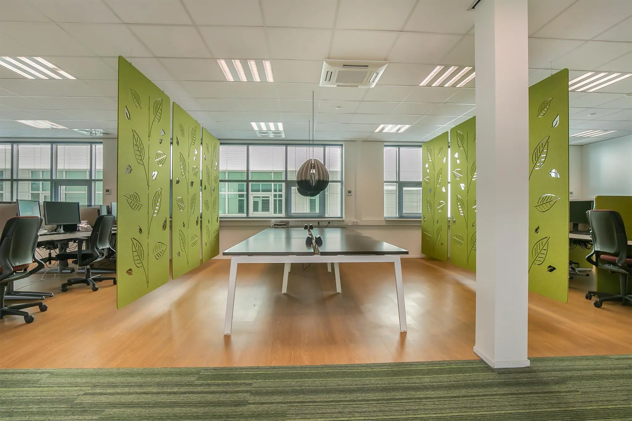 Moderne kantoorruimte met een tafeltennistafel in het midden, omringd door groene scheidingswanden met bladdesign.