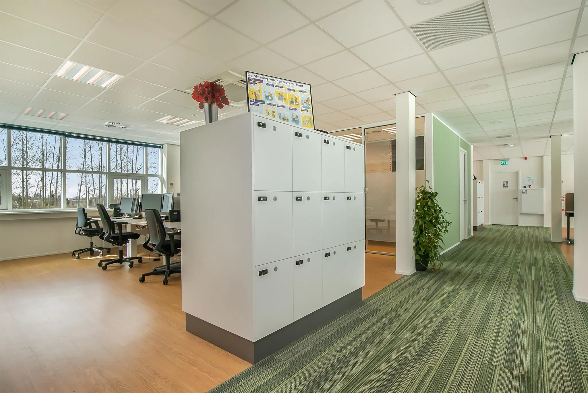 Modern kantoorinterieur met werkplekken, lockerkasten en een glazen vergaderruimte in het Rhijnspoor-gebouw.