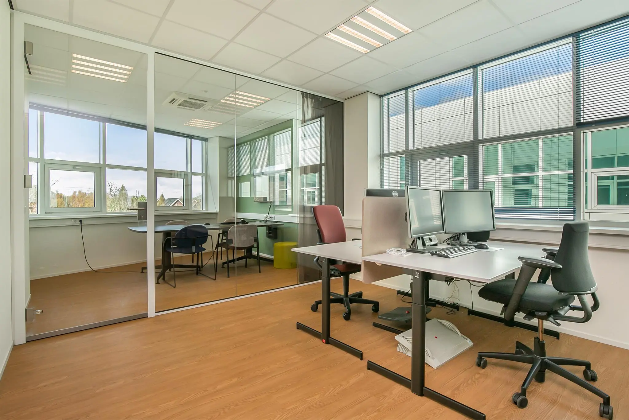 Modern kantoorinterieur met werkplekken, glazen vergaderruimte en grote ramen aan het Rhijnspoor.