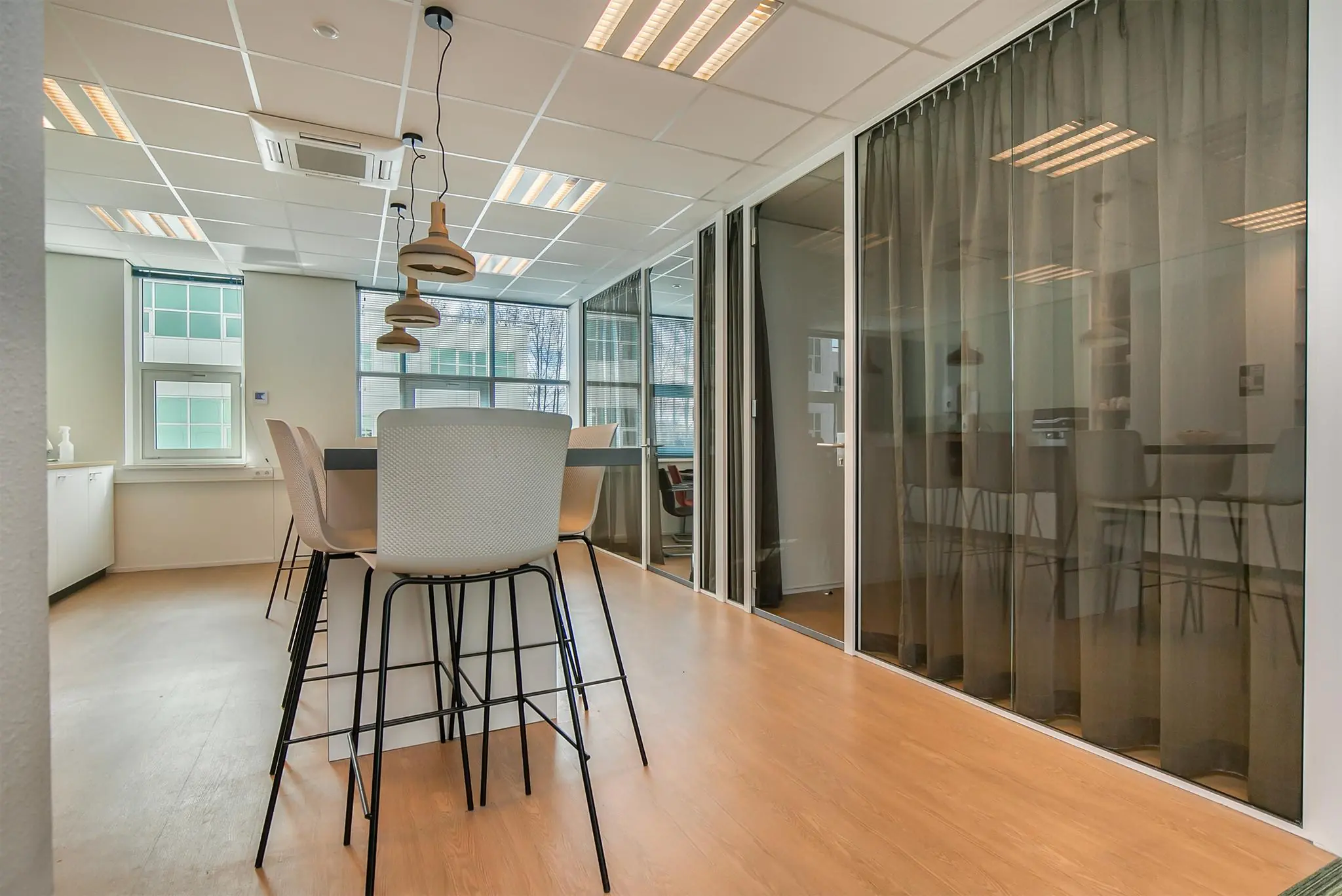 Moderne vergaderruimte in kantoorpand aan het Rhijnspoor met hoge stoelen, hanglampen en glazen wanden met gordijnen.