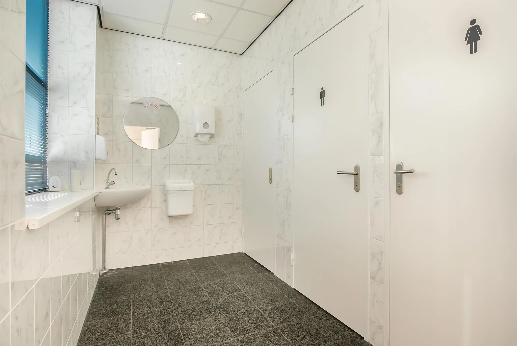 Moderne, betegelde sanitaire ruimte met twee toiletdeuren en een wastafel bij Rhijnspoor.