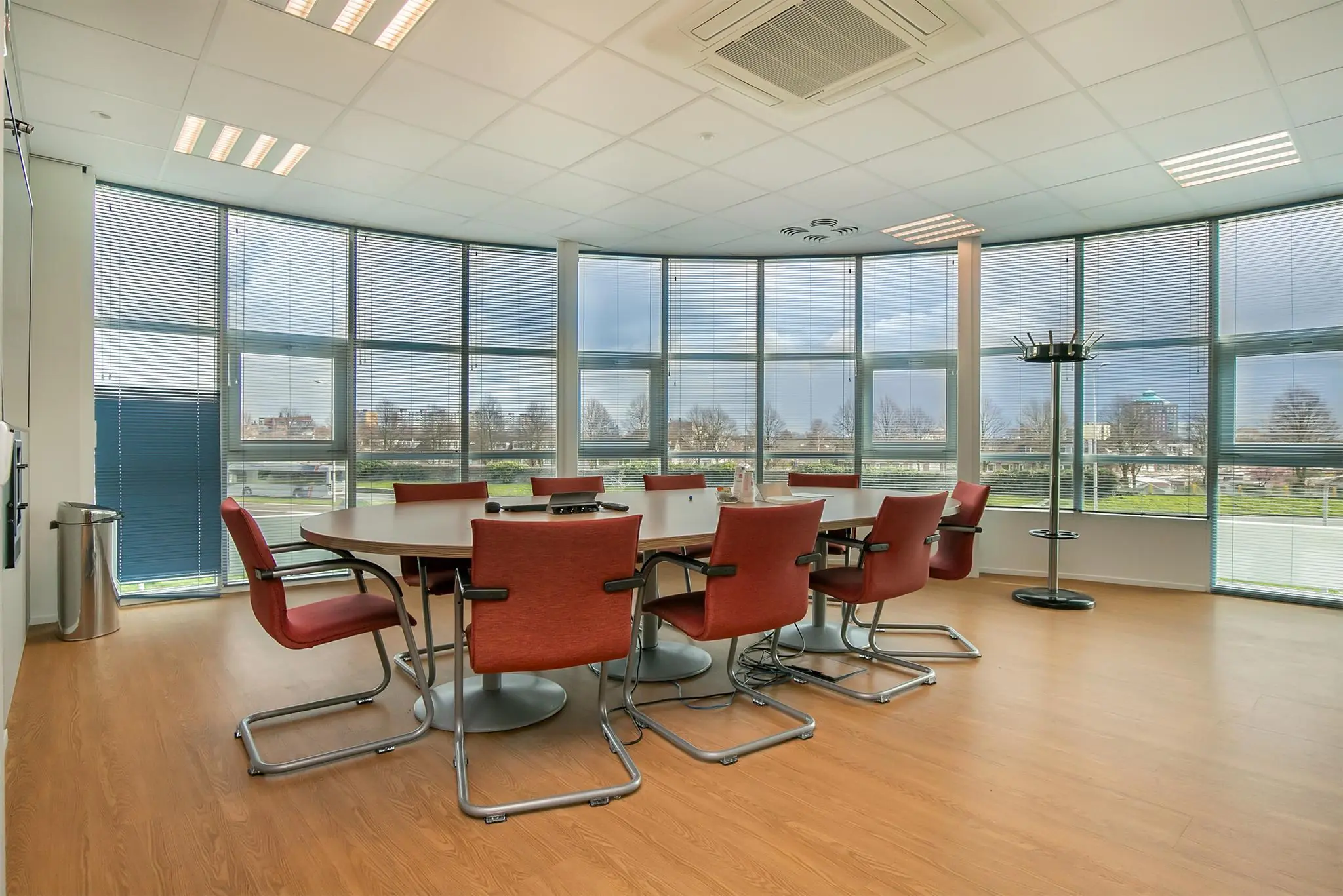Vergaderkamer met roodbruine stoelen rond een ovale tafel in een modern kantoorpand aan het Rhijnspoor.
