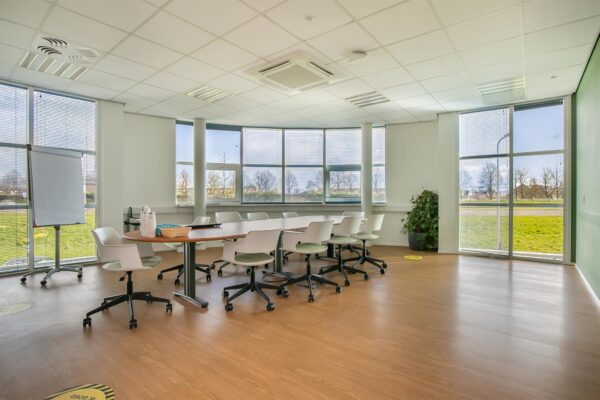 Vergaderruimte met grote ramen, een ovale tafel, witte stoelen en een flip-over in het Rhijnspoor-gebouw.