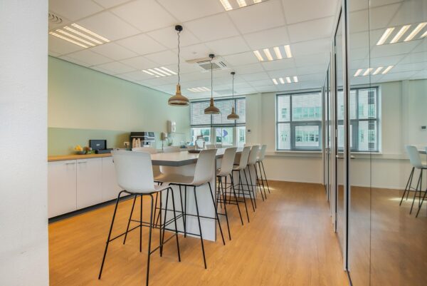 Moderne kantoor kantine met hoge stoelen, hanglampen en een lange tafel in het Rhijnspoor-gebouw.