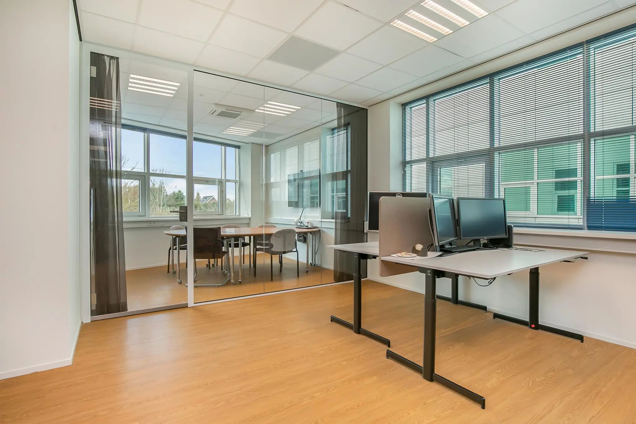 Moderne kantoorruimte in Rhijnspoor met glazen vergaderruimte en werkplekken met computeropstellingen.