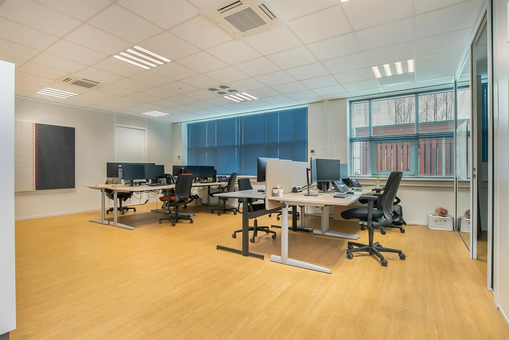 Moderne kantoorruimte aan het Rhijnspoor met meerdere werkplekken, bureaustoelen en computers, omgeven door grote ramen en glazen wanden.