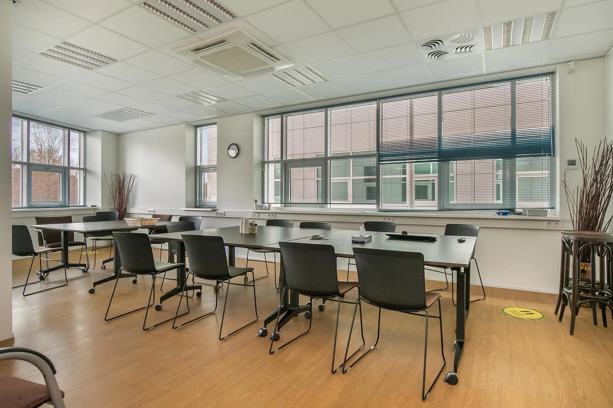 Vergaderruimte in het Rhijnspoorgebouw met meerdere tafels, stoelen en grote ramen.
