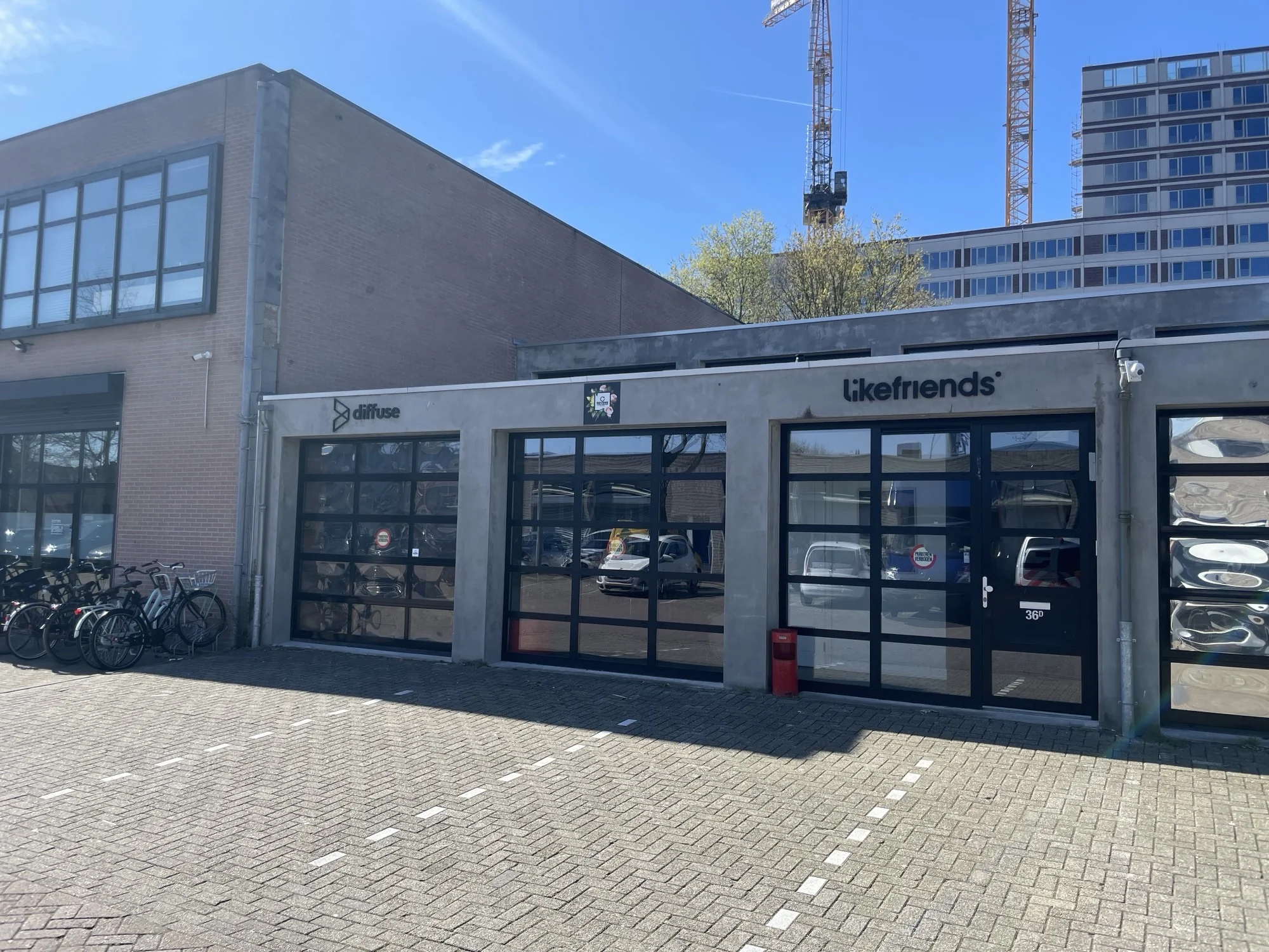 Bedrijfsgevels van Diffuse en Likefriends aan de Veemarkt met glazen deuren, geparkeerde fietsen en een blauwe lucht op de achtergrond.