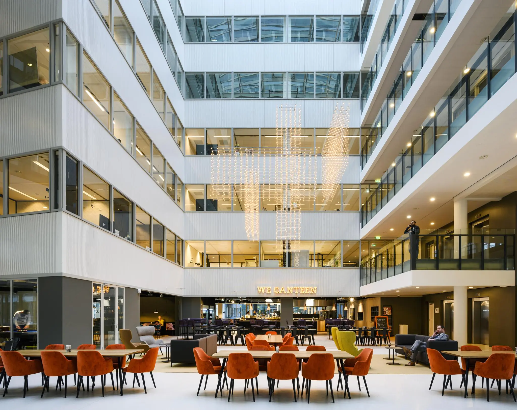 Moderne, open kantoorlobby aan de Thomas R. Malthusstraat met zithoeken, eetgedeelte en opvallende verlichtingsinstallatie.