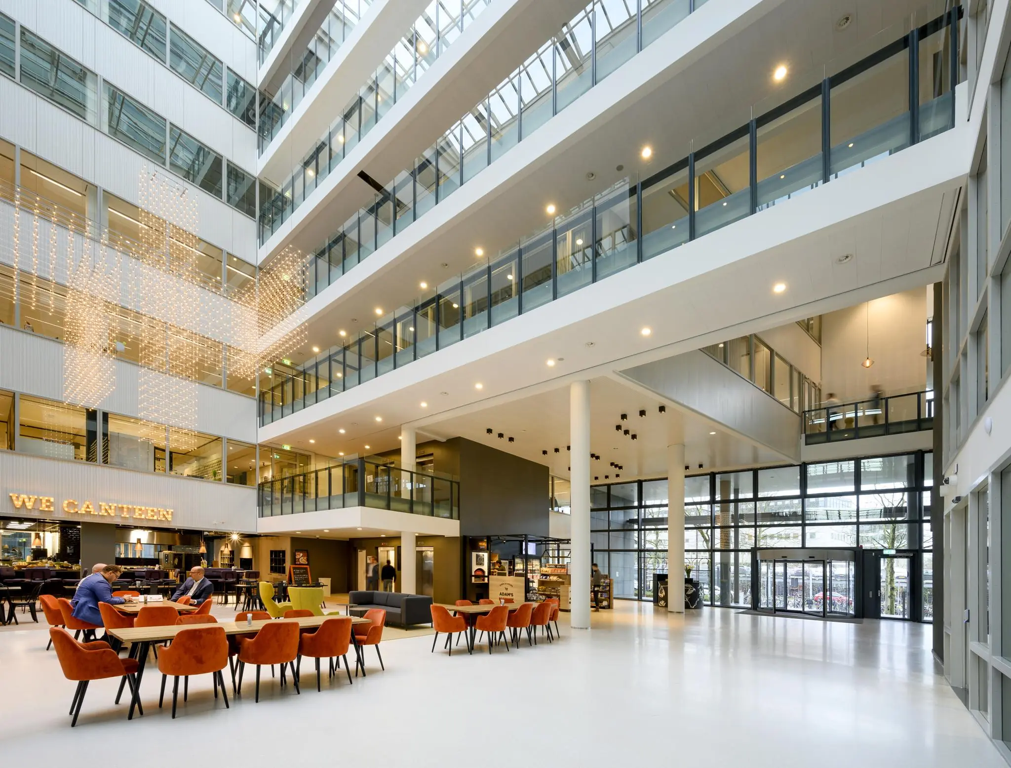 Moderne en lichte kantoorlobby aan de Thomas R. Malthusstraat met zitruimte, eetgelegenheid en glazen gevel.