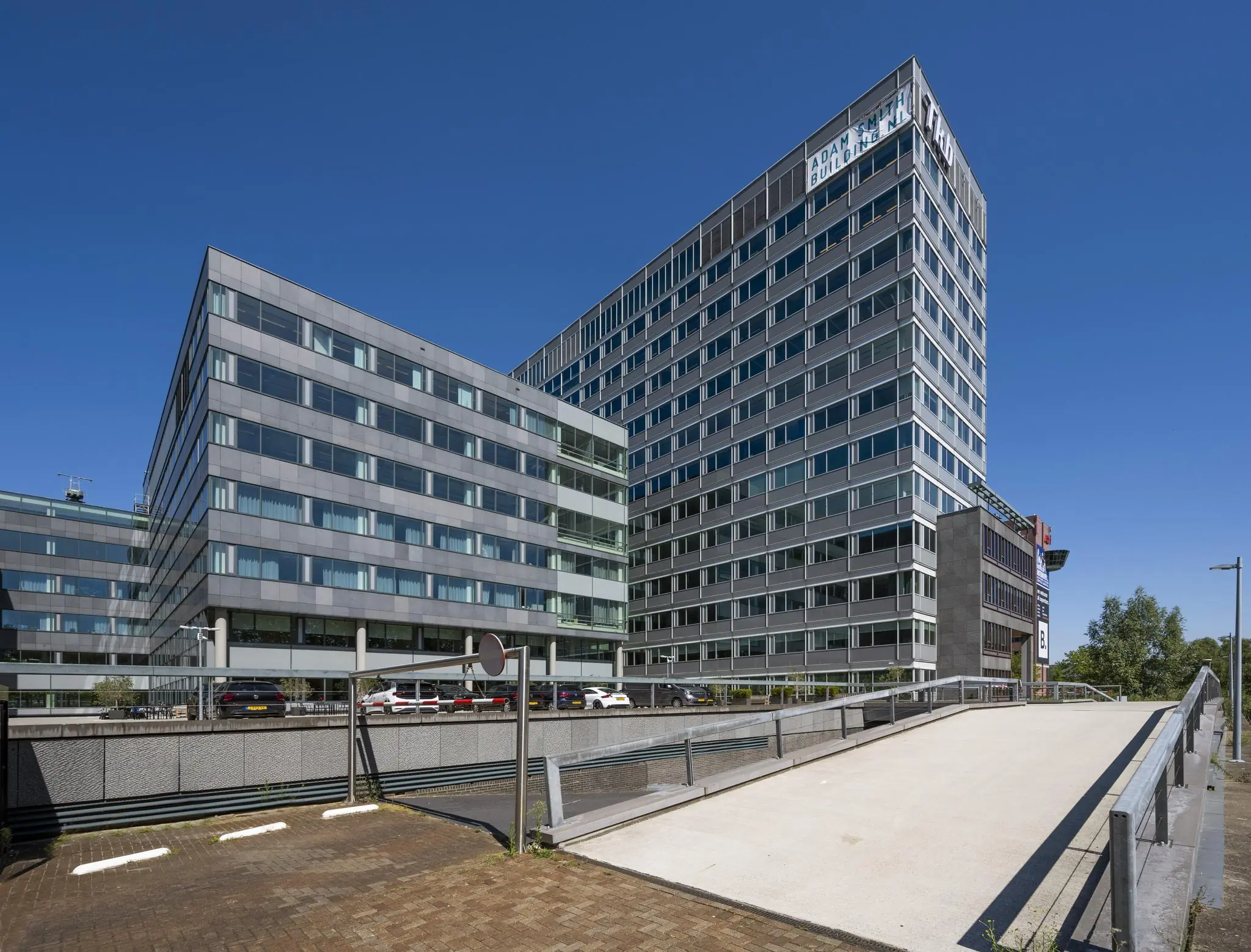 Modern kantoorgebouw aan de Thomas R. Malthusstraat in Amsterdam met glazen gevel en oprijbrug op de voorgrond.