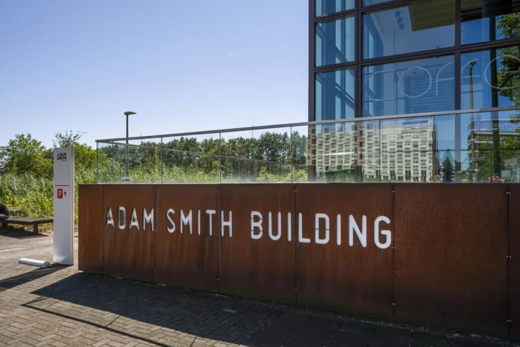 Vooraanzicht van het Adam Smith Building aan de Thomas R. Malthusstraat met moderne gevel en naambord.